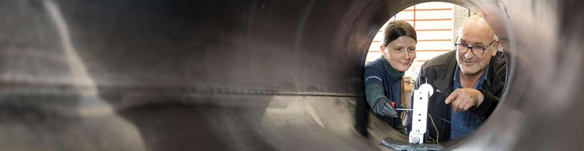 View from inside a pipeline of two employees looking at a device inside the pipeline.