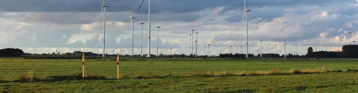 A landscape with wind turbines and pipeline markings in the foreground.