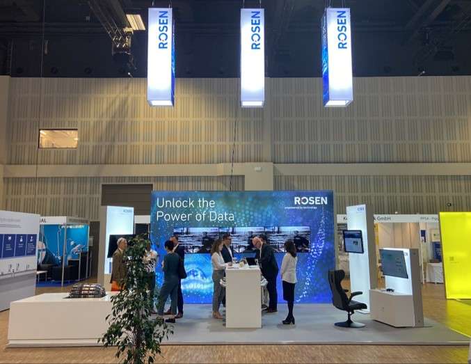 This image shows the ROSEN booth at the PTC 2024 from the front. A group of people can be seen standing at the booth.