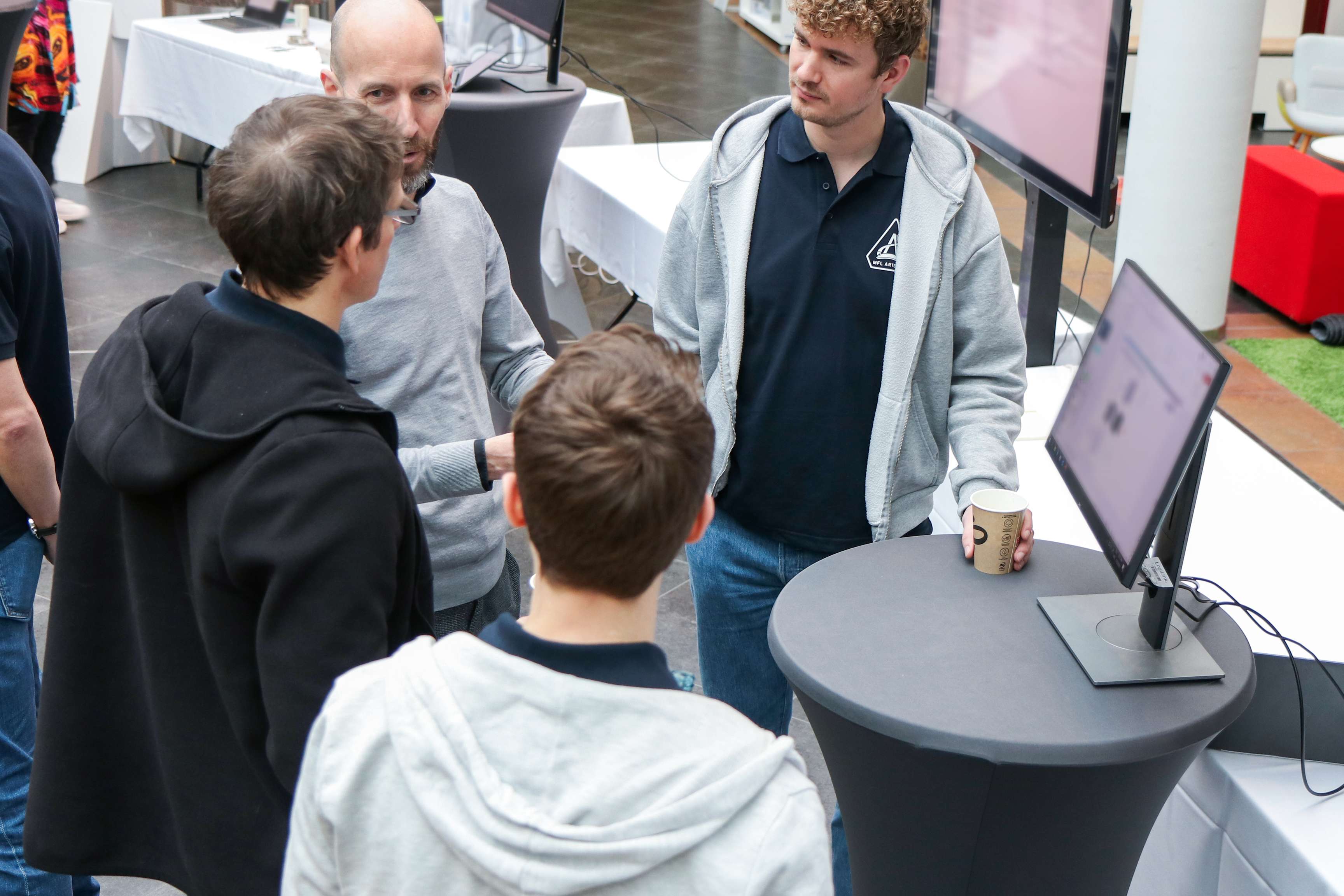 A group of men are standing around a PC and discussing with each other.