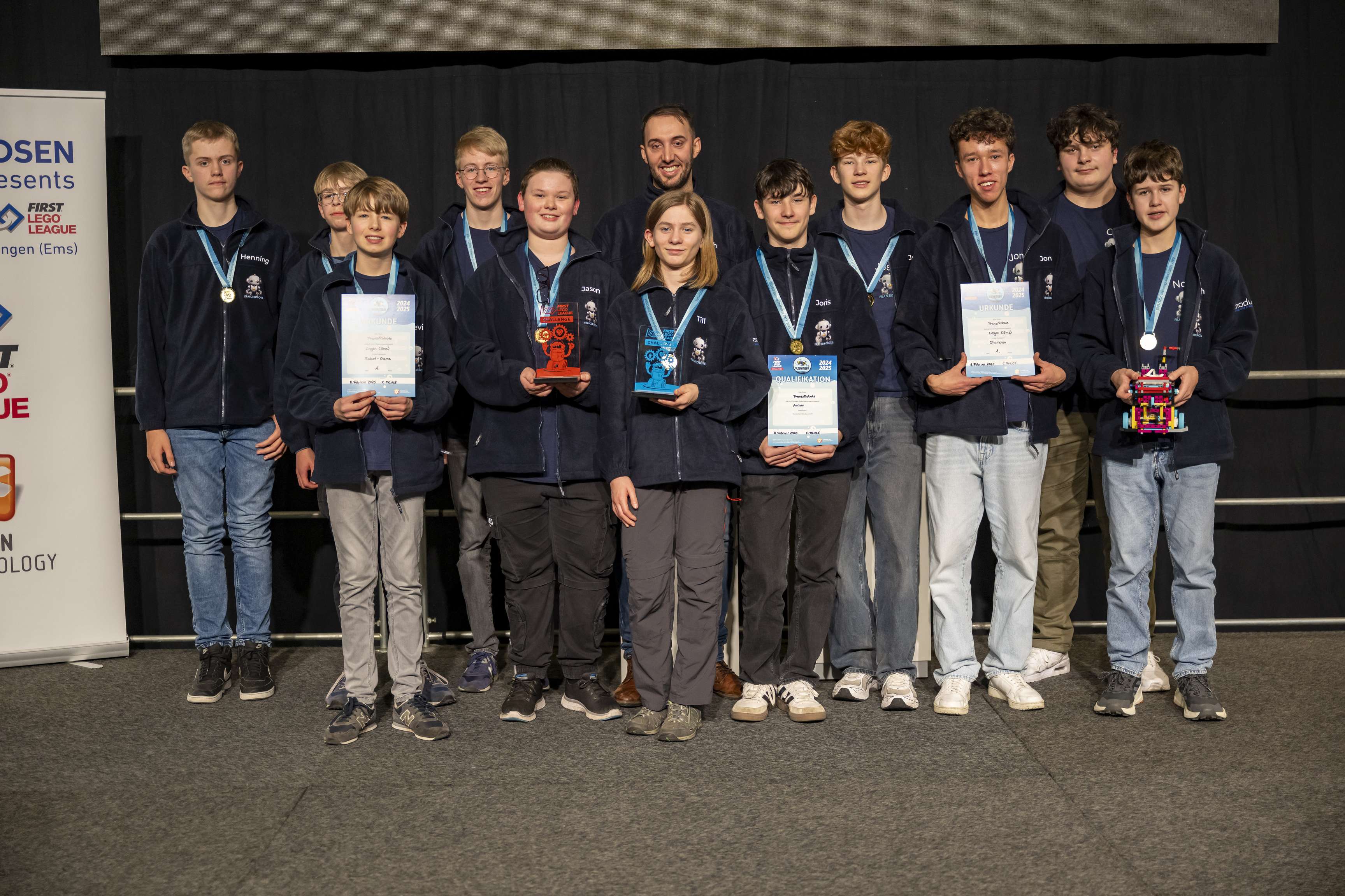 The FIRST LEGO League winners pose for a group photo. They hold trophies and certificates in their hands.