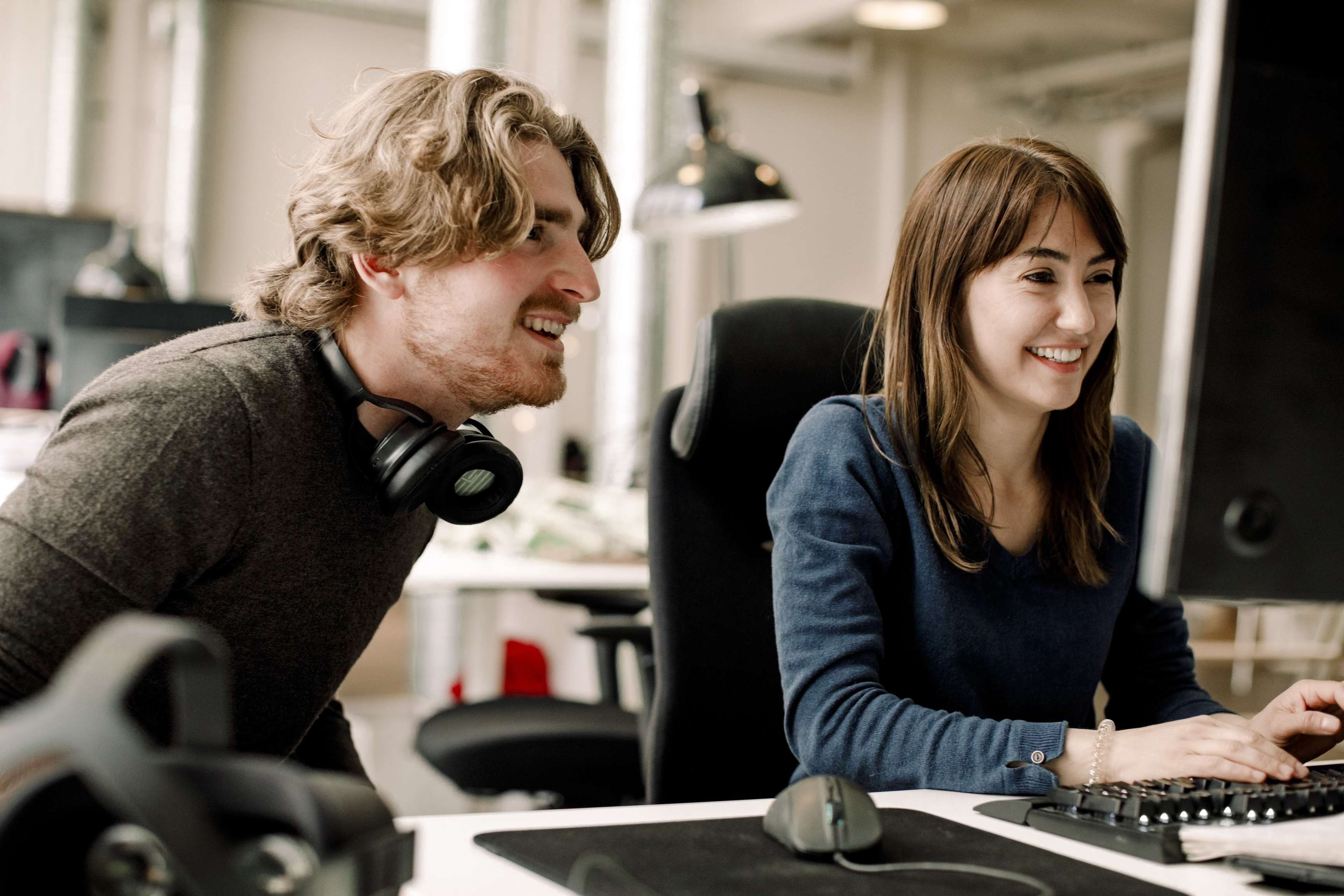Male and female professionals smiling and sitting in front of a computer in the office discussing.