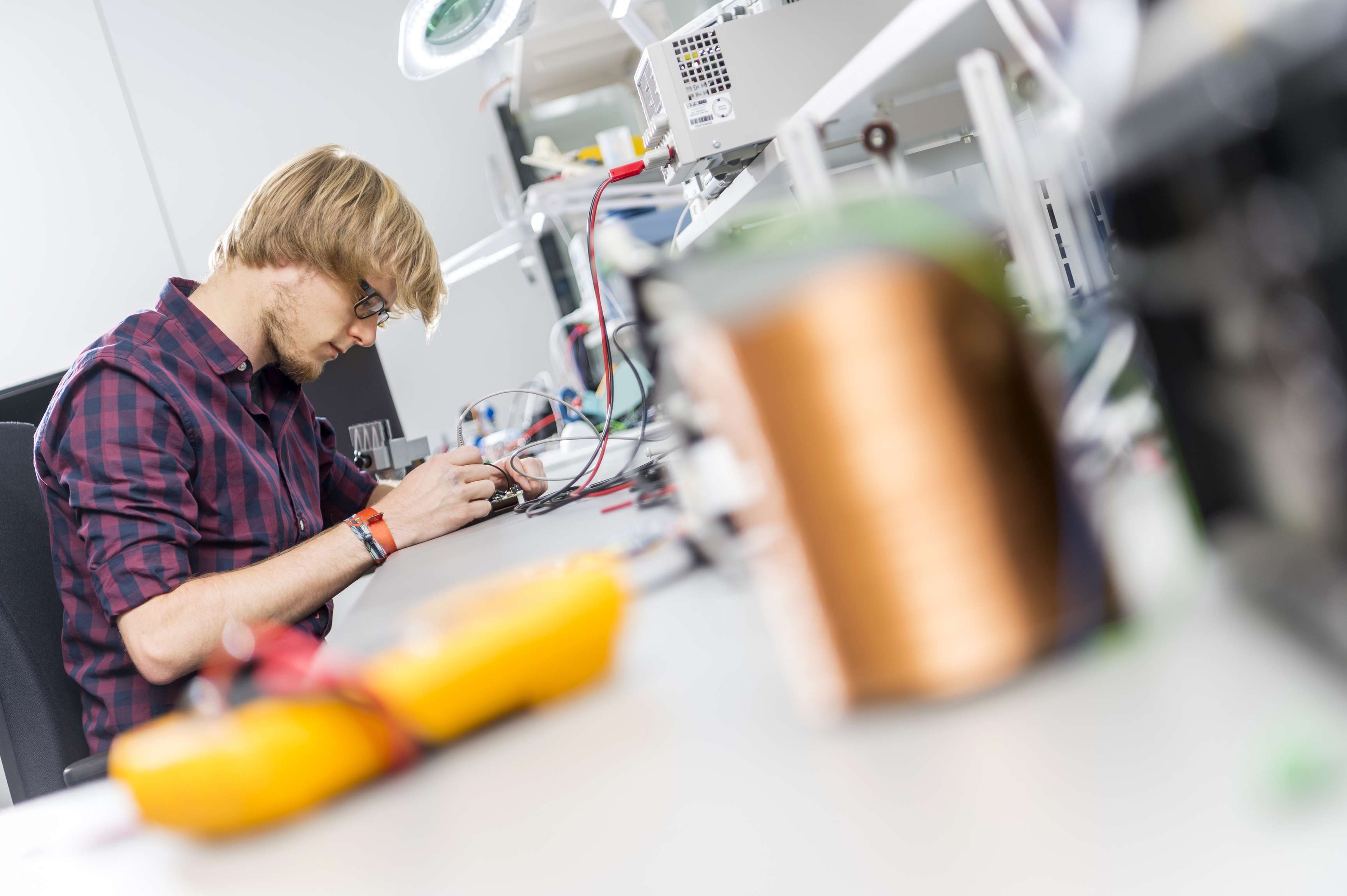 Employee works at a table on a device from which cables lead to a machine.