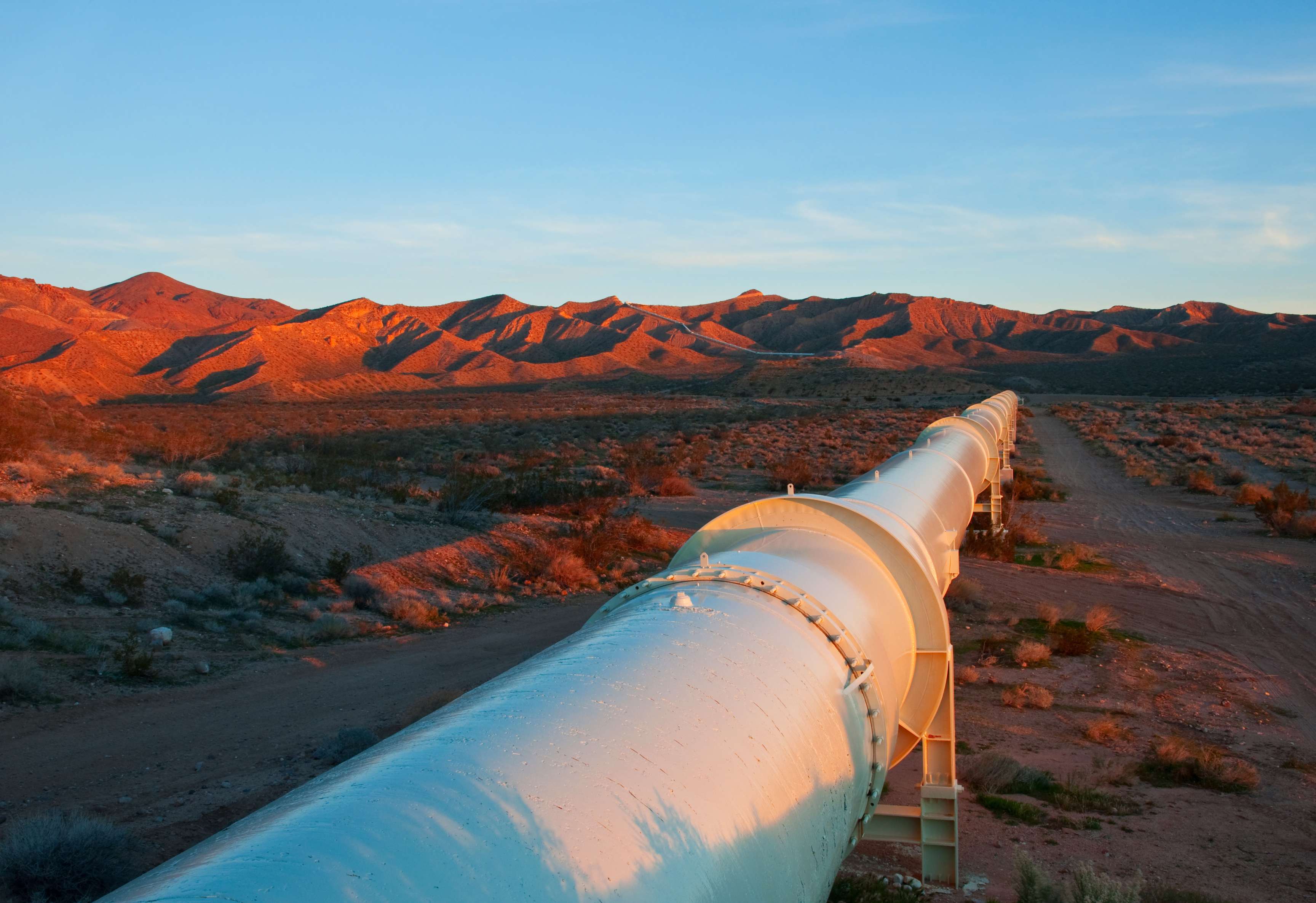Pipeline leads through dry hilly landscape at sunset.
