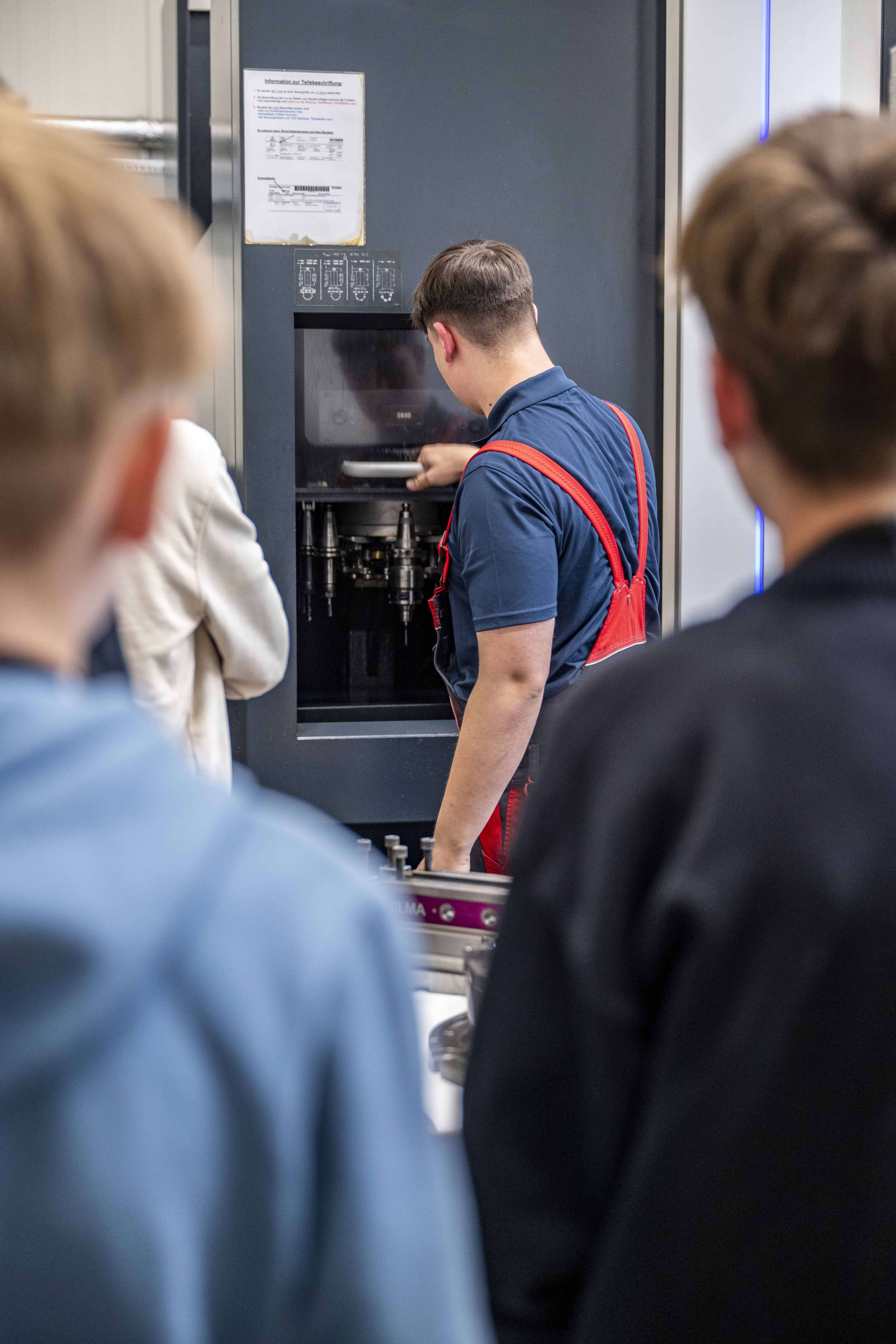 Ein Auszubildender bedient eine Industriemaschine, während eine Gruppe im Rahmen eines praktischen Workshops zusieht.