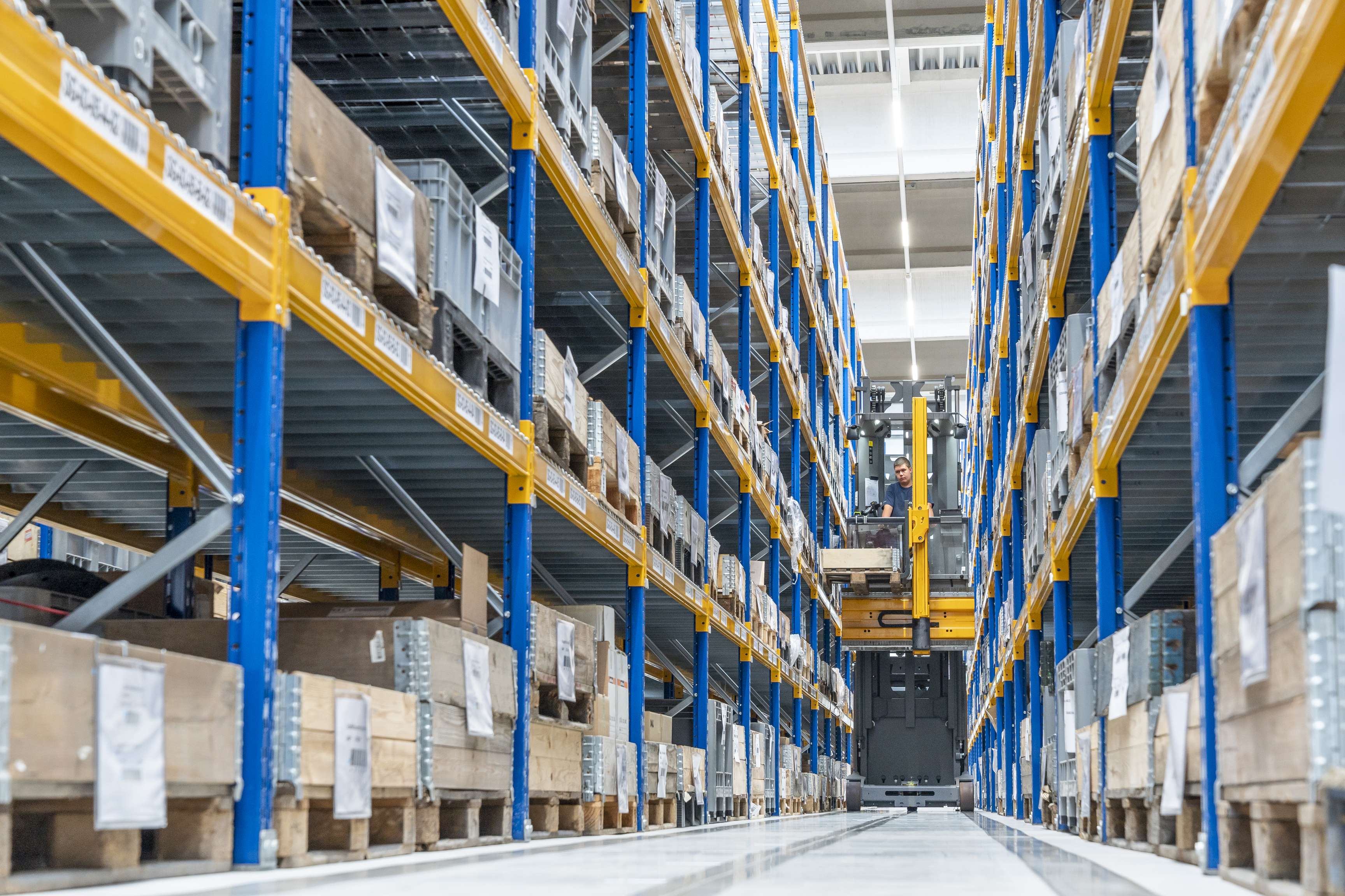 Ein Gabelstapler fährt zwischen Hochregalen hindurch.