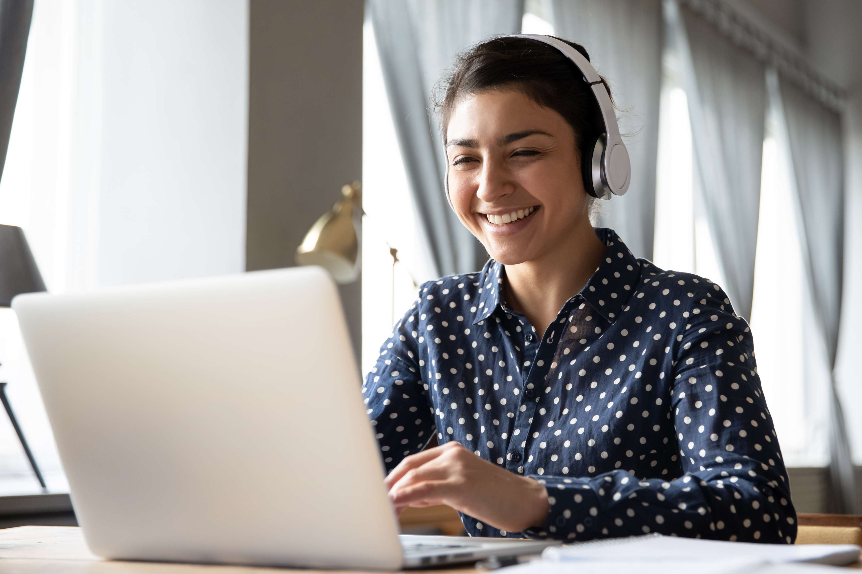 Woman smiling with headset on sitting in front of laptop.