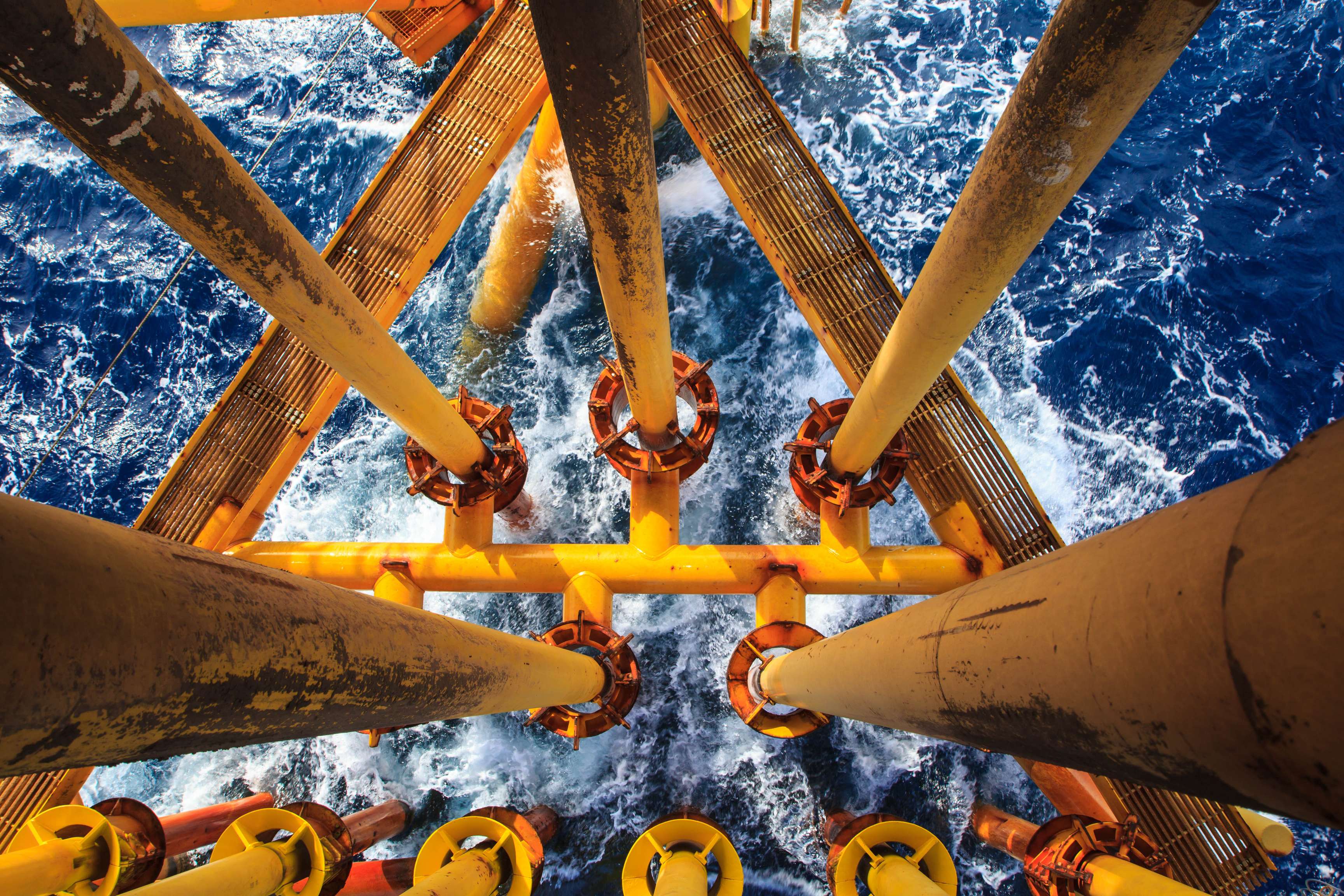 Bird's eye view of vertical yellow pipelines leading into the rough ocean.
