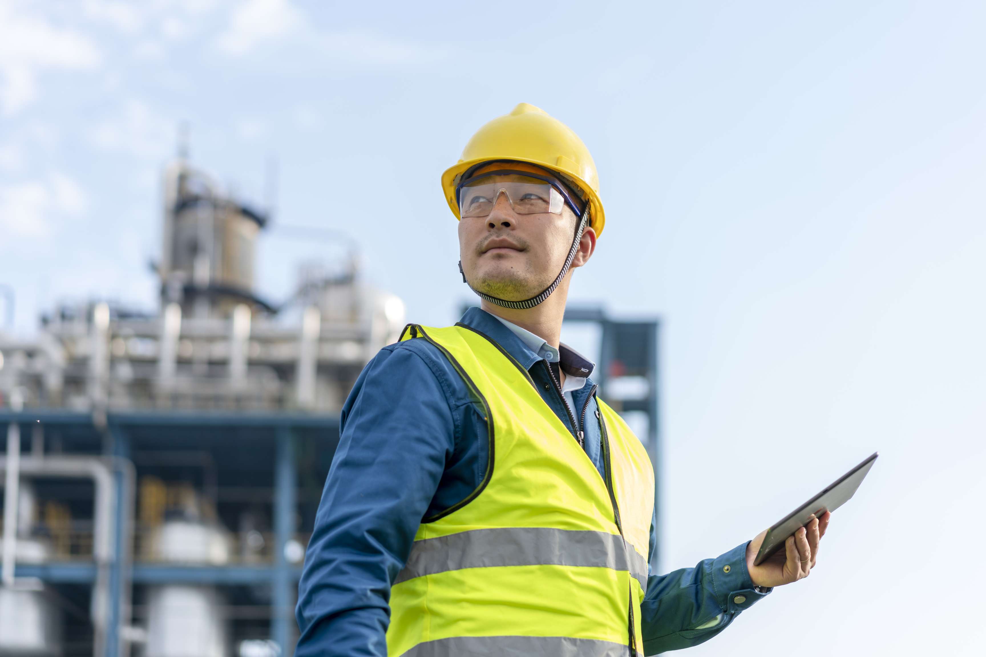 Employee wearing helmet and high-visibility vest with clipboard in hand.