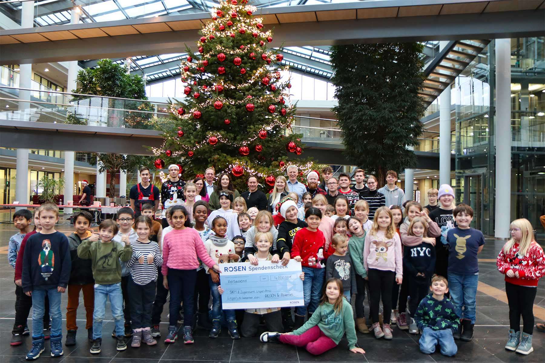 Many people (children and adults) in front of a Christmas tree at the donation handover.