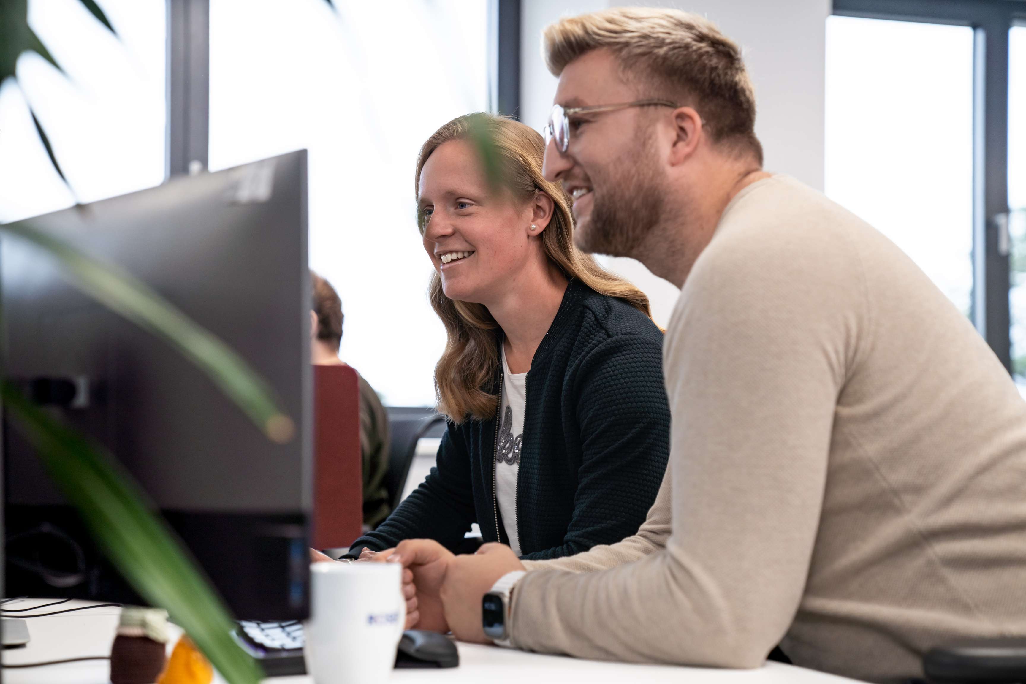 Ein Mann und eine Frau, die zur Seite auf einige Bildschirme schauen.