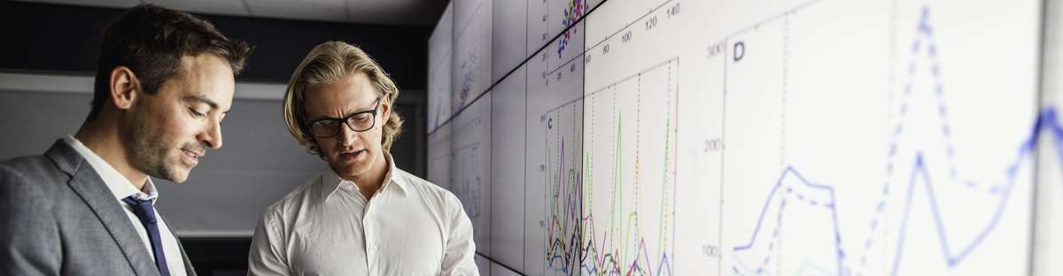 Group of business people in a dark room standing in front of a large data screen with information.