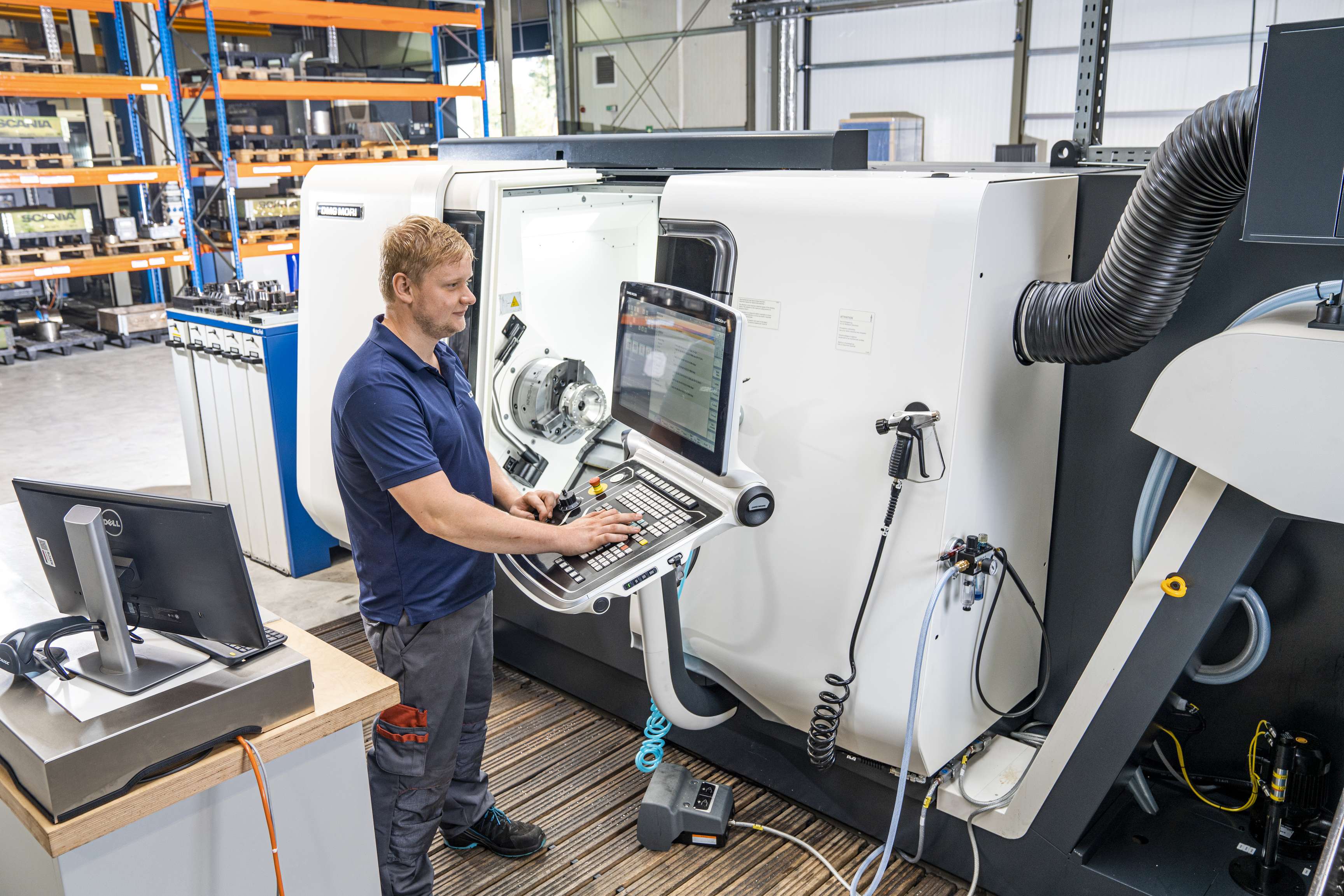 Ein ROSEN Mitarbeiter steht an einer hochkomplexen Maschine und bedient sie mithilfe eines außen angebrachten Monitors. Er trägt Arbeitskleidung und im Hintergrund sieht man Hochregale.