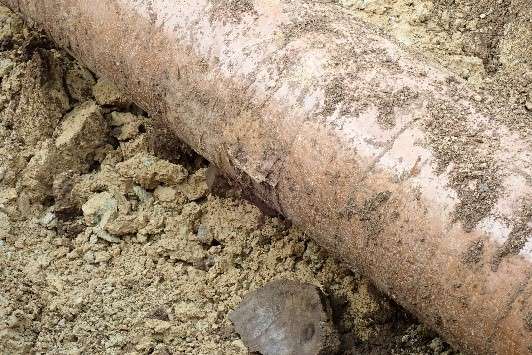 Picture of an excavated, single-layer polyethylene (PE) tape pipe with a coating defect where the coating is easily detached and visible slight surface corrosion.