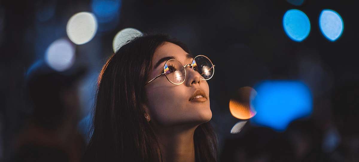 Woman wearing glasses looking to the right with a dark background.