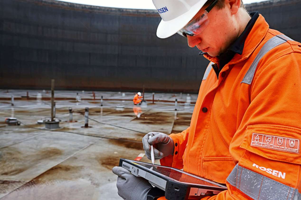 ROSEN expert in an orange jumpsuit in a tank without a roof working on a tablet.