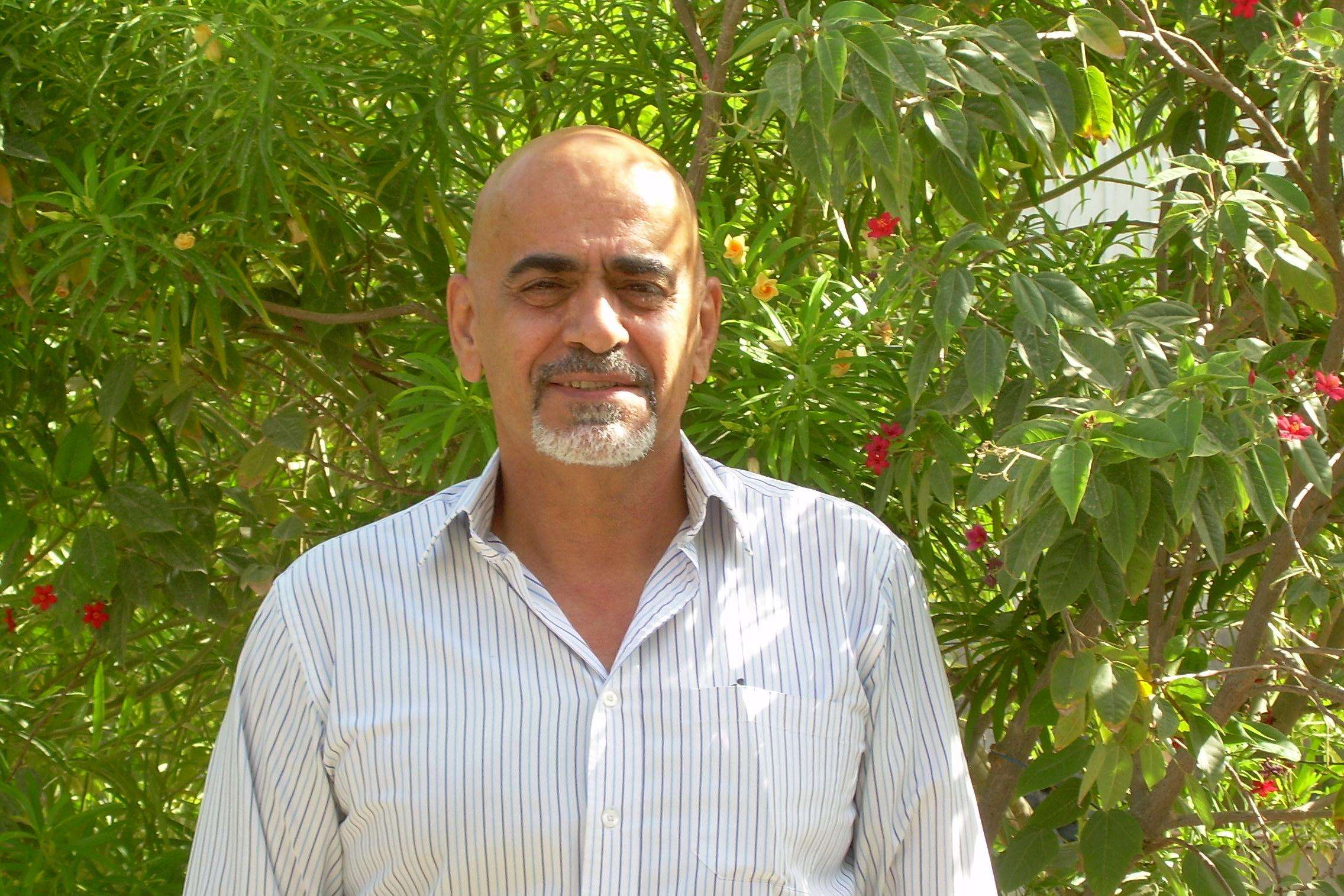 Man smiling into camera as portrait standing in front of leaves.