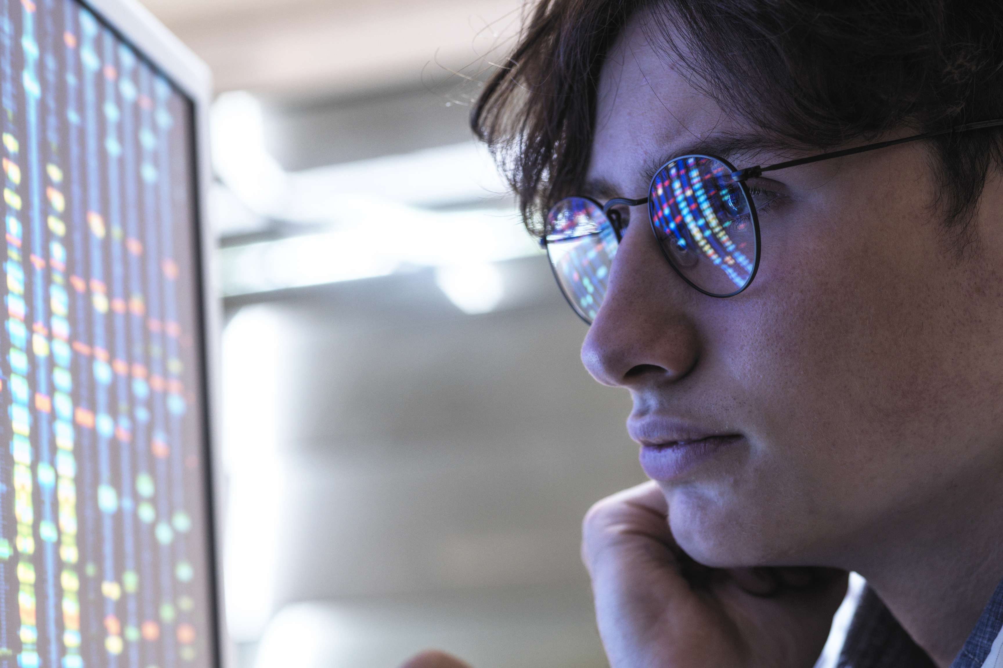 A man wearing glasses in front of a screen, holding a ballpoint pen while analyzing data.