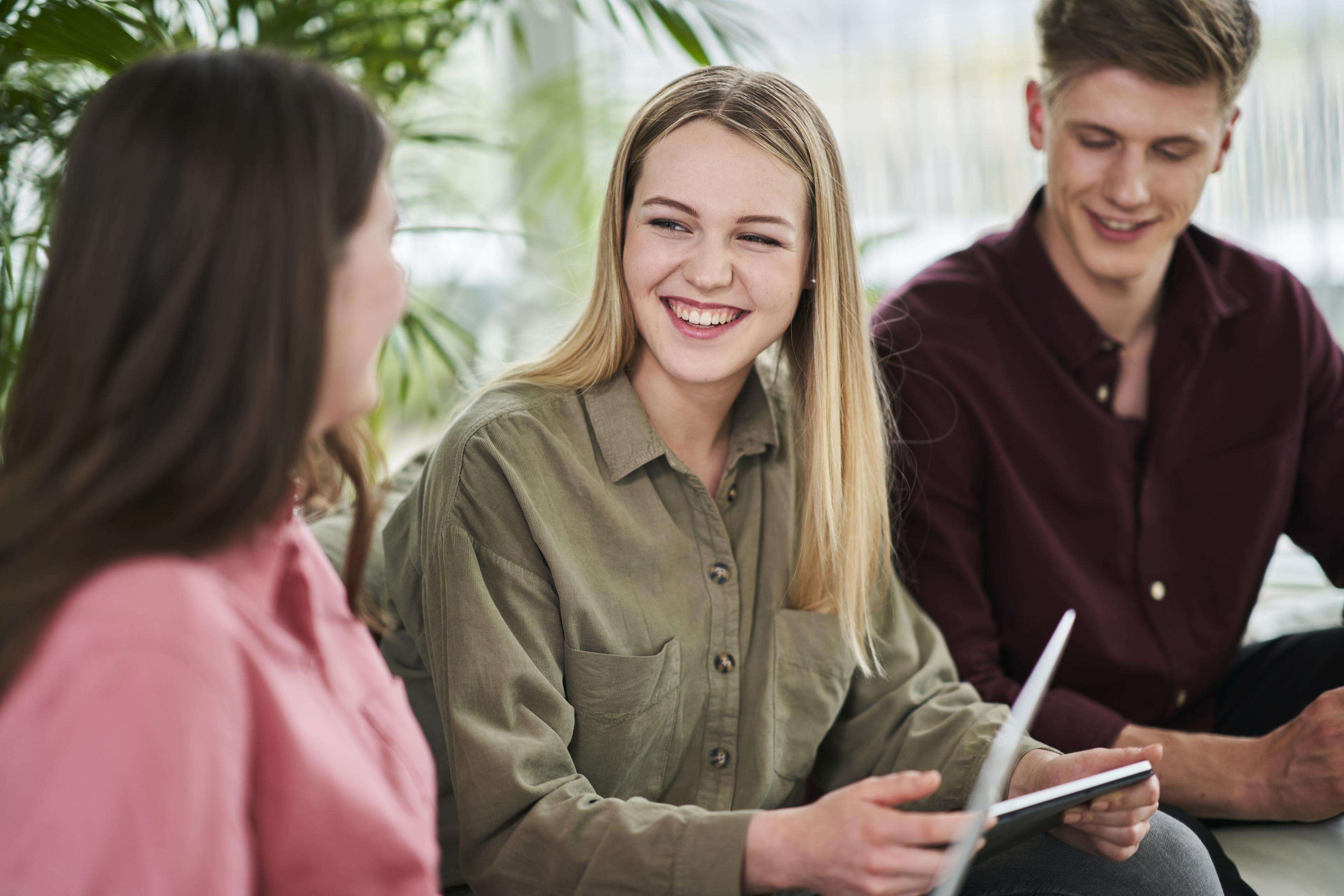 A young smiling woman sits with a young man and another woman.