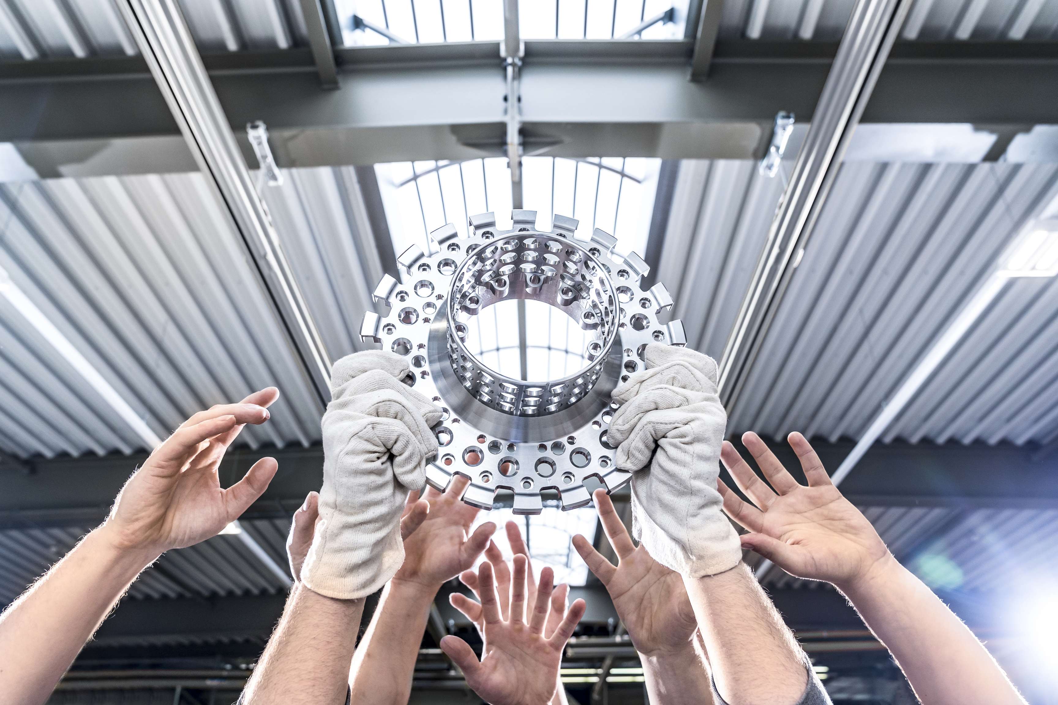 Viele Hände hielten ein maschinell hergestelltes Stahlteil hoch.