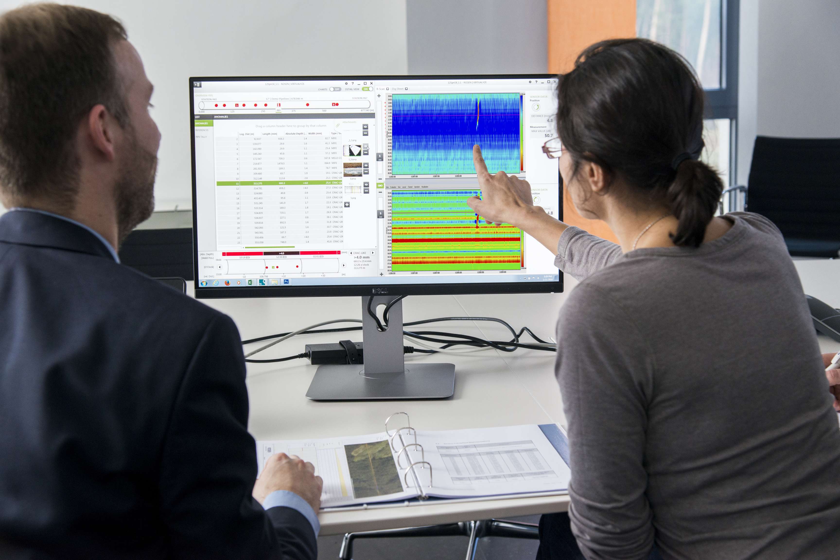 Two employees looking and pointing at graphs on computer screen.
