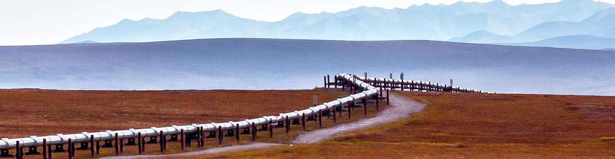 Image of above ground pipeline going through flat landscape with mountains in the background.