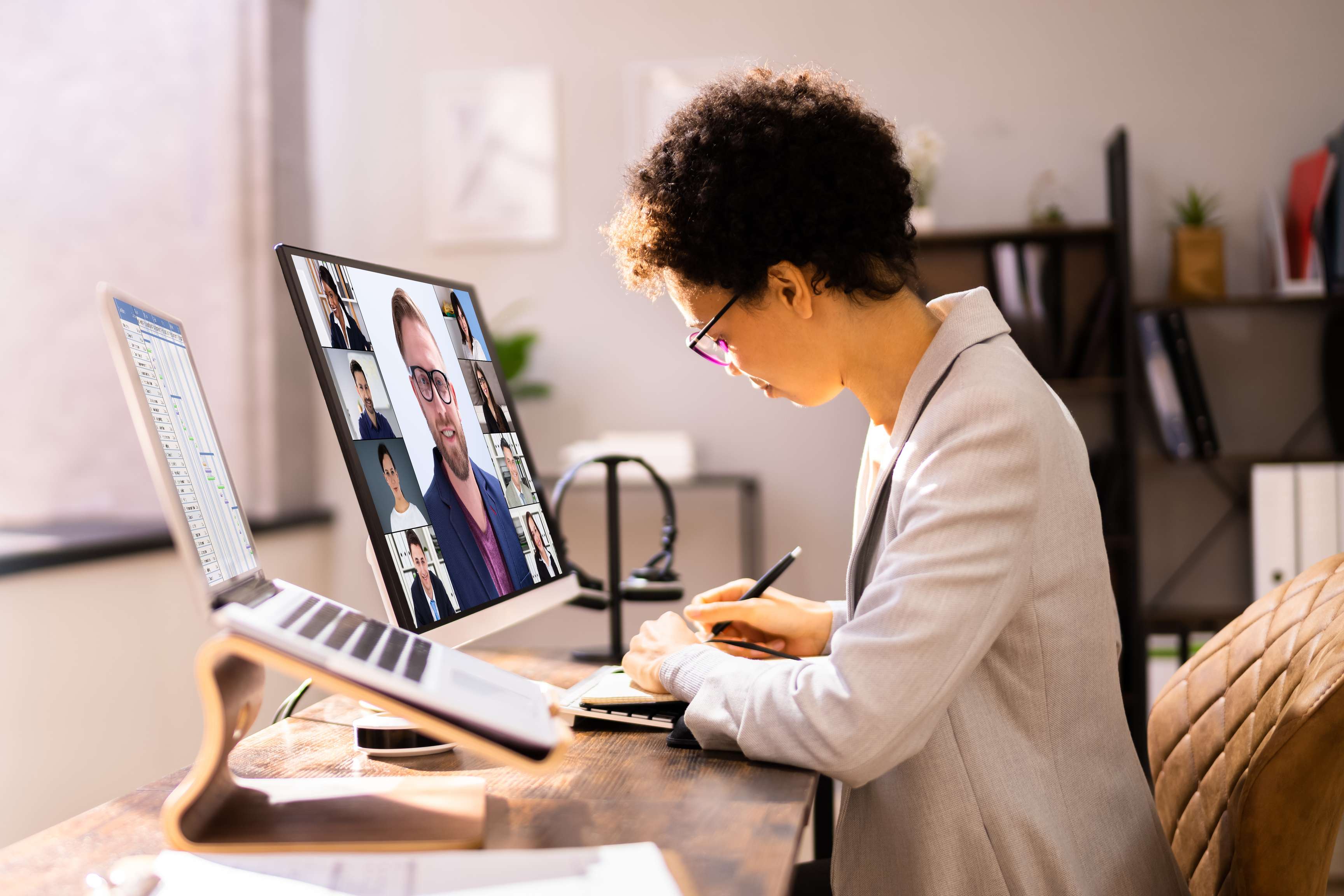 Woman taking notes while sitting in front of a laptop in an online meeting.