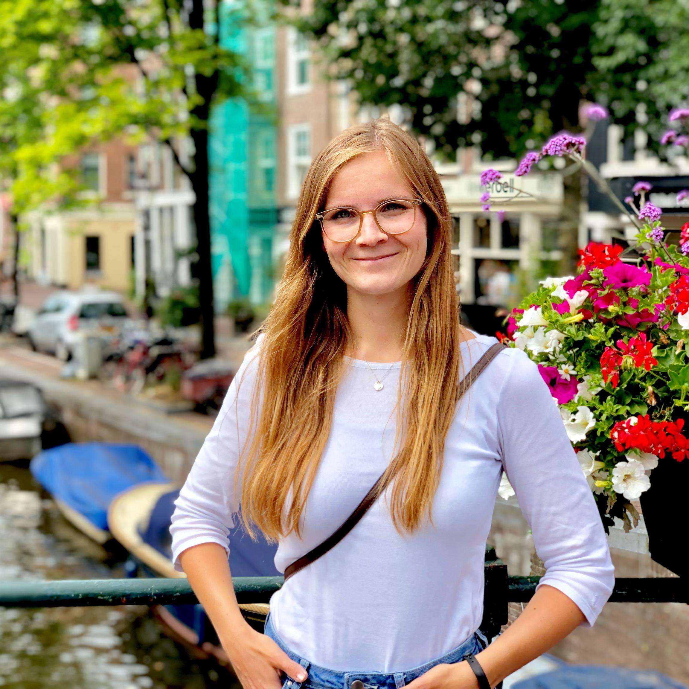 Young smiling woman with glasses in front of canals in Amsterdam.