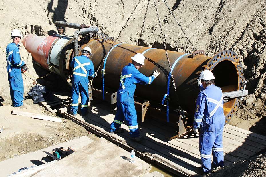 Several workers at a pipeline opening in a pit.