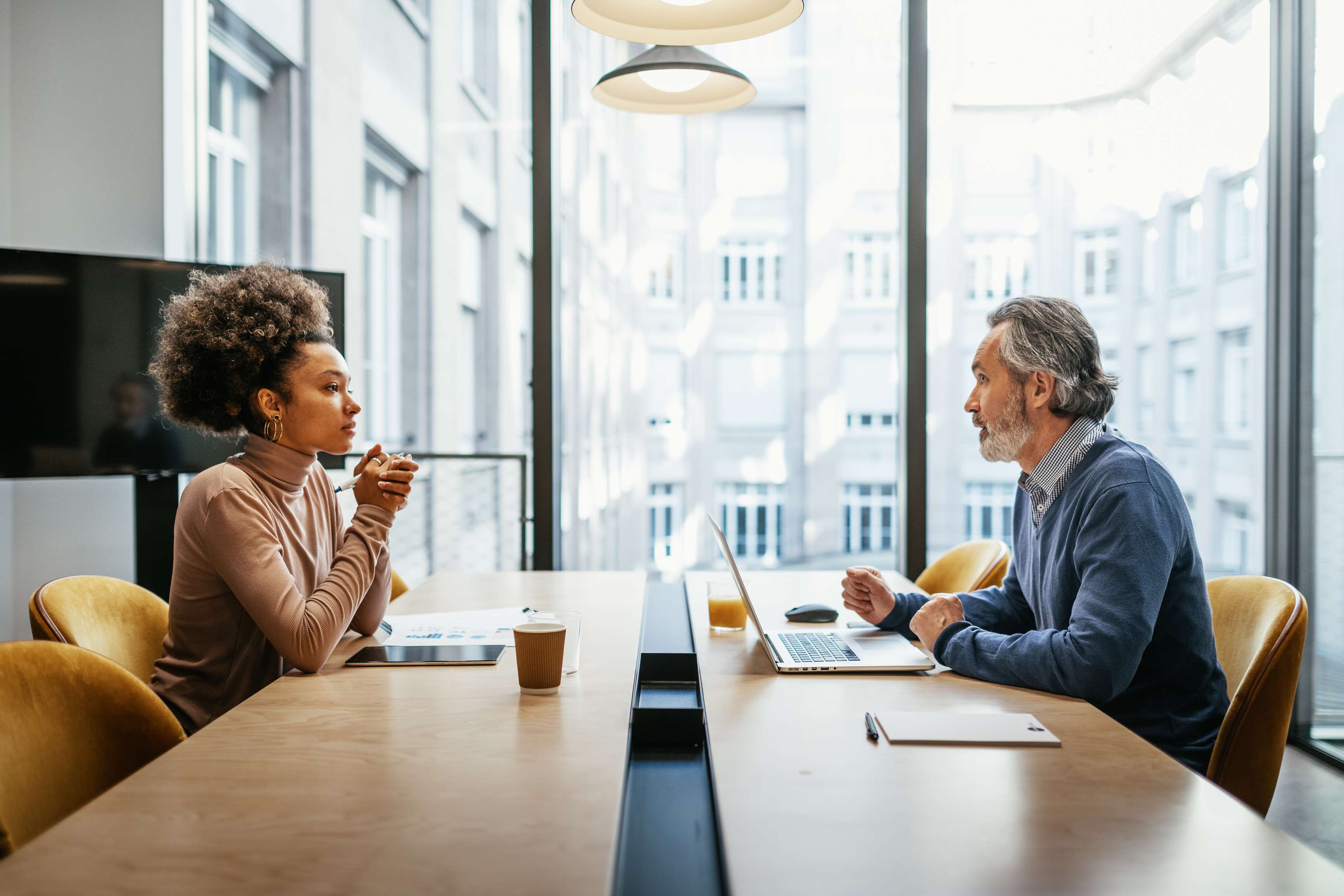 Two employees in a meeting room sitting in front of each other and talking.