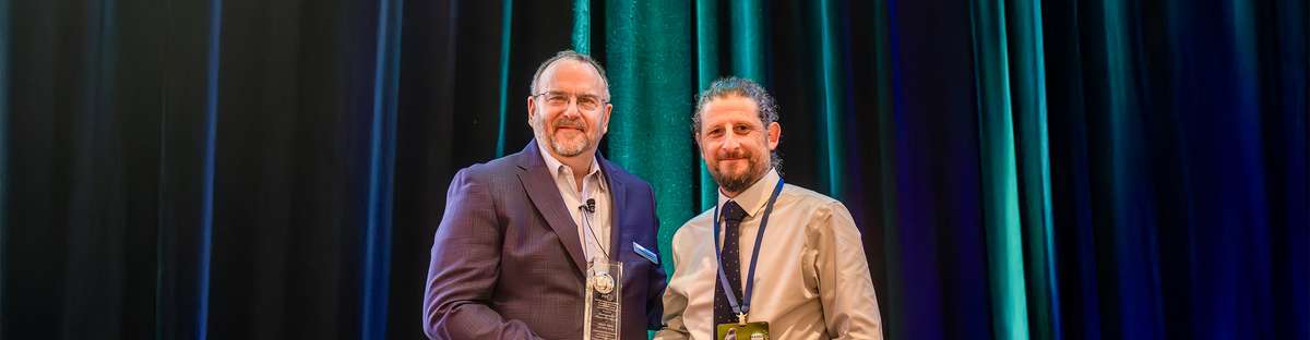 This photo shows the ceremonial presentation of the PRCI Researcher Award to Simon Slater on stage.