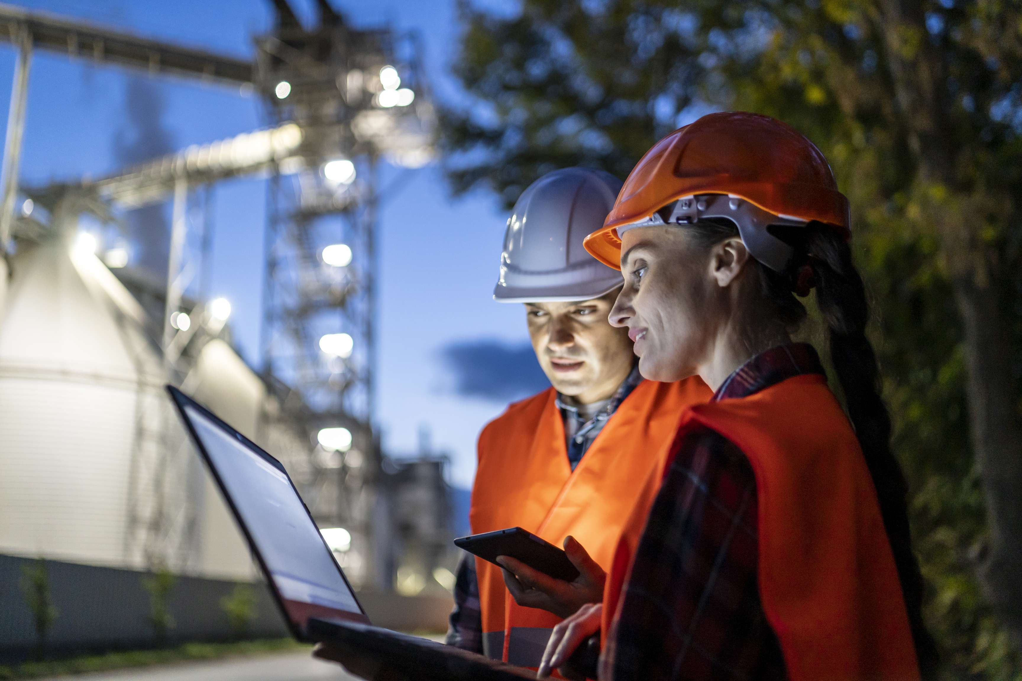 Female and male engineer during night shift in factory using a tablet and a laptop.